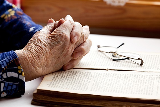 A pair of hands folded with glasses and a book.